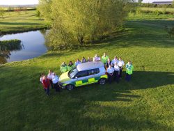 The Vale Responders team stood around a community responder car, taken from above with a drone
